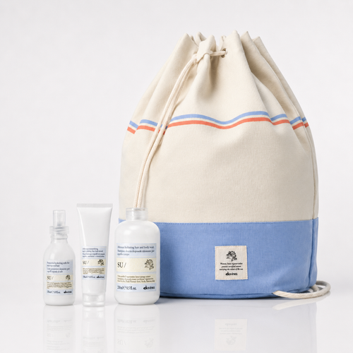 Fotografia del set di prodotti Davines SU/ con tre flaconi cosmetici bianchi una sacca beige e azzurra a strisce rosse e blu e etichetta logo su sfondo bianco